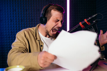 expressive and emotional radio host with headphones reading news from paper into studio microphone...