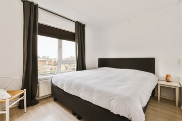 a bedroom with white walls and black curtains on the windowsilling there is a bed in front of the...