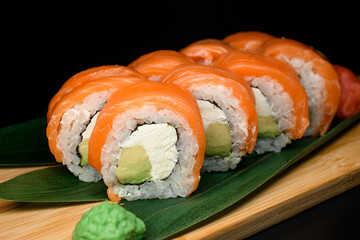 Appetizing Philadelphia sushi rolls on wooden board served with green plant leaves, ginger and wasabi