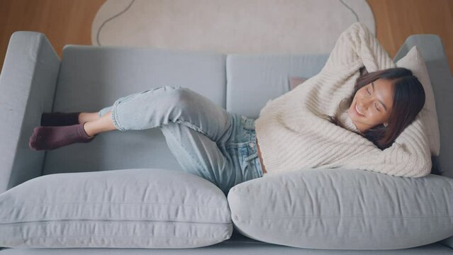 Top view - Happy young asian woman falling on huge comfortable couch and relaxation in living room, Enjoying carefree weekend.