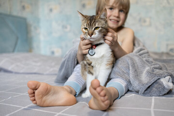 boy holds a cute domestic cat between his bare feet while sitting at home in the morning on the bed. Communication and tender atmosphere between beloved pet and child. selective focus