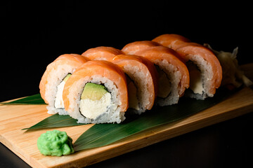 Pieces of tasty Philadelphia sushi rolls on wooden board served with green plant leaves and ginger
