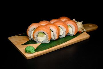 Pieces of fresh Philadelphia sushi rolls on wooden cutting board served with fresh leaves, spicy wasabi and ginger