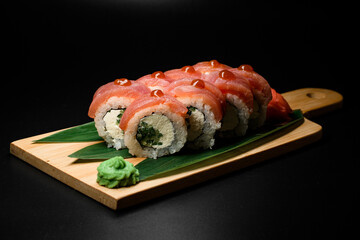 Appetizing view of pieces of Philadelphia tuna sushi roll with cucumber, cream cheese and drop of teriyaki sauce on wooden board served with banana leaves and wasabi