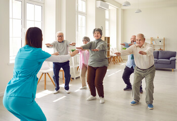 Senior group doing squat exercise with physiotherapist in gym. Elderly men and women having physiotherapy class, rehab course with trainer guide. Elderly people healthy lifestyle - obrazy, fototapety, plakaty