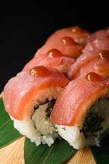 Pieces of Philadelphia tuna sushi rolls with drop of teriyaki sauce served on wooden board on black background