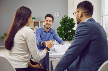 Happy caucasian couple sitting back and having consultation with a young attractive man realtor or...