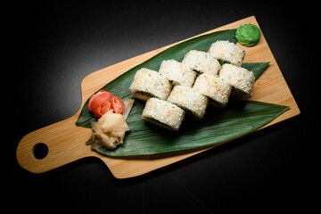 Horizontal view of vegetarian California sushi rolls served on wooden board decorated with banana leaves, ginger and wasabi