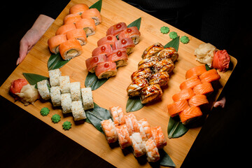 Woman holds large serving board with Philadelphia and California set Sushi Rolls with fresh fish, vegetables and cheese inside.