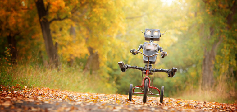 Happy humanoid robot rides a bicycle along the autumn alley. Robotic object experiences feelings and emotions. Concept of technology development in the form of artificial intelligence.