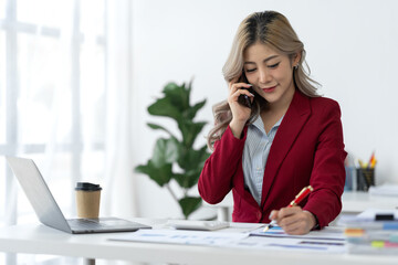 Attractive Asian businesswoman using mobile phone to search, contact, chat, business negotiations with customers. Online paperwork at office desk.