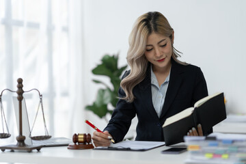 Attractive and confident asian female lawyer holding pen working in office with contract and legal book while sitting at table. Law, legal services, advice, justice and real estate concept.