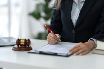 Attractive and confident asian female lawyer holding pen working in office with reading contract documents and law books while sitting at desk. Law services, advice, justice and real estate concept.