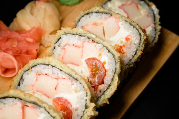 Tasty hot tempura sushi with shrimp, vegetables and philadelphia cheese on wooden serving board. Closeup view