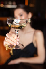 a girl holds a glass wine glass with alcohol in the foreground