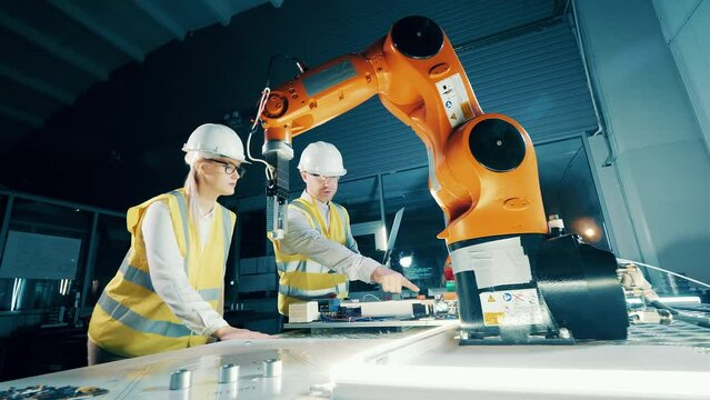 Two engineers in hardhats working with modern robot