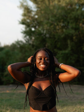 A young black woman with braids, touches her hair, feels beautiful, and enjoys the sun during a sunset stroll