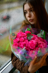 beautiful woman leans on window and holds large bouquet of colorful fresh roses