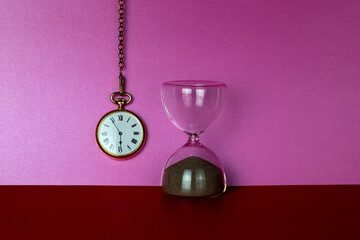 Hanging Gold Pocket Watch with Sand Glass Timer on a Red Surface and Pink Background