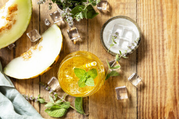Melon lemonade in glasses with ice and mint on a wooden rustic table. Fresh refreshing fruity summer drink, seasonal beverages. View from above. Copy space.