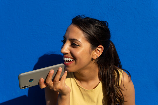 Smiling young ethnic woman using smartphone against blue backdrop