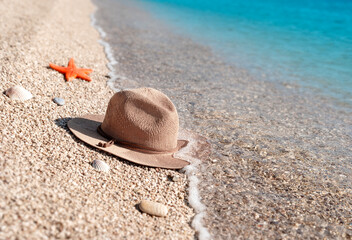 Fototapeta na wymiar A straw hat lies on the beach near the water with starfish and seashells