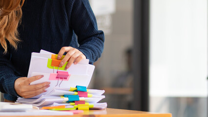 secretary searches through stacked paperwork on desk in office to find lease within stacked paperwork just before meeting. concept difficulty in finding hire purchase contract from stacked paperwork