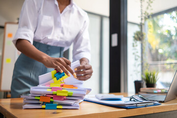 secretary searches through stacked documents on desk in office to find lease within stacked documents just before meeting. concept difficulty in finding hire purchase contract from stacked documents