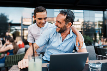 Fototapeta na wymiar Handsome and happy father and his teenager son sitting in a restaurant and talking.