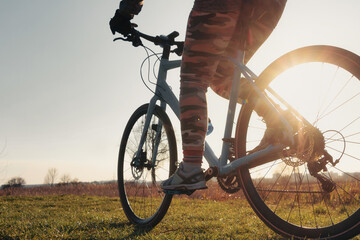 Close-up of a girl on a bicycle riding on green grass against setting sun background. Sports lifestyle, cycling training.