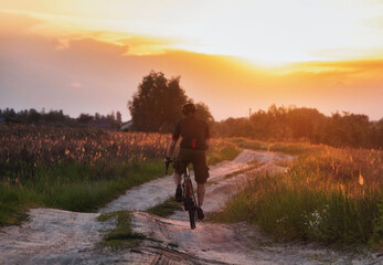 Fototapeta premium Cyclist riding a trail in a field on a gravel bike on a dramatic sunset background. Sport and active lifestyle concept.