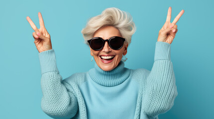 Elderly stylishly dressed woman showing peace sign on fingers on blue background.
