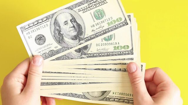 A small stack of one hundred dollar bills. Money in hands on a yellow background, top view. The concept of investment, business, money exchange or payout