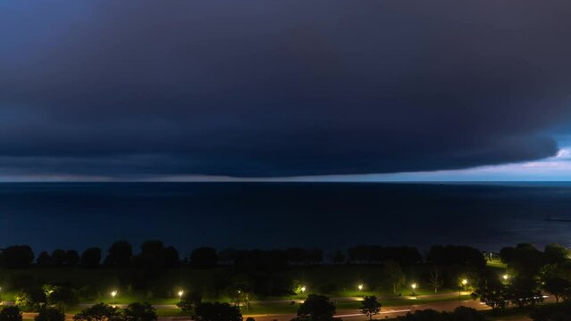 A storm time lapse of a dark cloud mass rolling in over Lake Michigan as a weather front blankets the sky at night with traffic lights streak across Lake Shore Drive in the foreground.