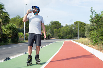 Male inline skater drinking water from a stainless steel bottle on a bike lane.