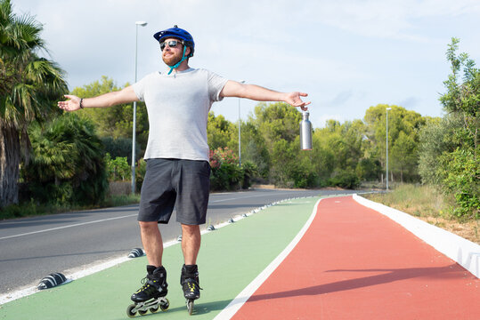 Man practising inline skating with arms outstretched on a on a bike lane.