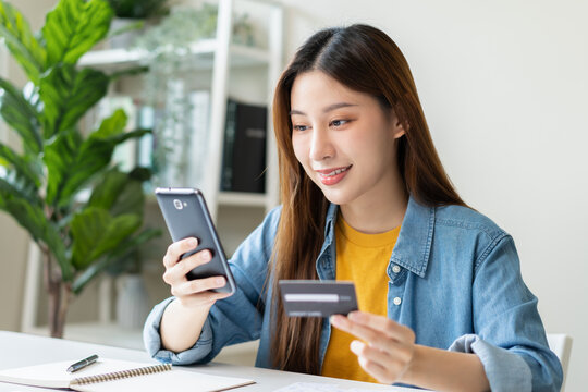 Online internet banking, smile asian young woman hand holding credit card to payment spending, using mobile phone scan qr code to transfer or pay money without cash at home. Technology of financial.