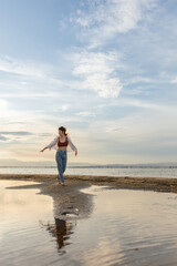 woman on the beach dancing at sunset in backlight with the sun behind in shadow, woman on vacation walking on the sand with golden water reflections from the sun at sunset