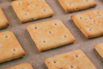 Spicy square crackers on parchment paper. Salty crackers closeup. Macro shot.