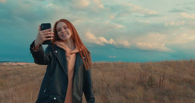 charming happy red-haired woman taking selfie for memory, picture nature beauty Girl using smartphone showing victory gesture while standing on beautiful landscape in autumn Slow motion Body language