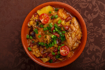 hot cholent sprinkled with green onions in a clay plate on a tablecloth.