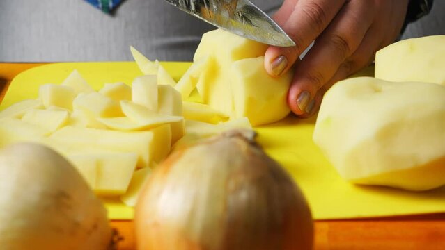 Female hands cut potatoes for cholent with a large knife on a plastic board