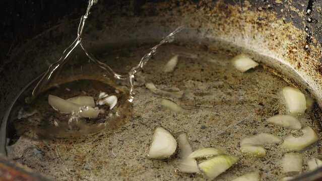 Finely chopped onions are poured into vegetable oil in a cast-iron frying pan heated over a fire