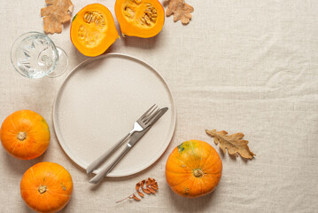 Autumn table setting. Beige plate, cutlery, fresh pumpkins on a beige linen tablecloth. Top view,...