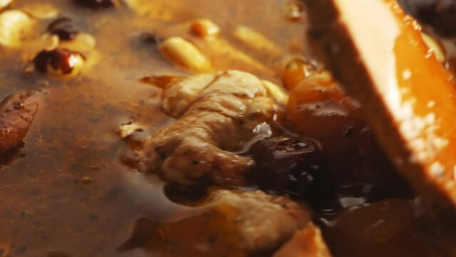Pieces of chicken fried in a cast-iron skillet in oil with onions and spices and dried fruits cholent are mixed with a spatula