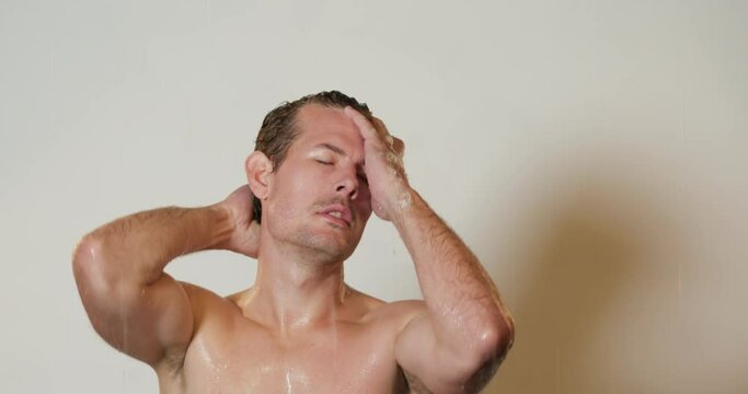 Happy sexy young Caucasian man enjoying singing taking morning shower. Smiling muscular hipster guy washing under warm water listening to music gets pleasure from hygiene routine in bathroom.