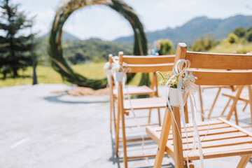 The wedding arch in the park is made of dry reeds on the background of the forest in blurred focus. Away wedding ceremony. Decorated chairs for the ceremony