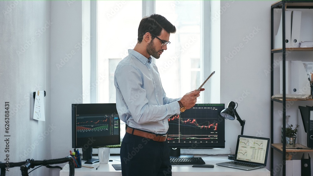Poster analyzing data. successful young trader in formal wear is looking at trading graphs and reports on h