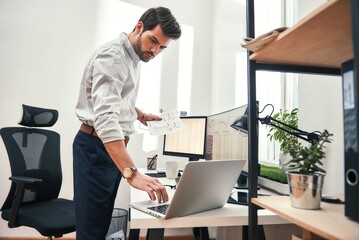 Multitasking. Side view of successful bearded trader or businessman in formal wear working with laptop while standing at his modern office.