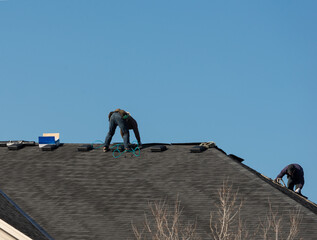Two roofing workers on the roof replacing asphalt shingles